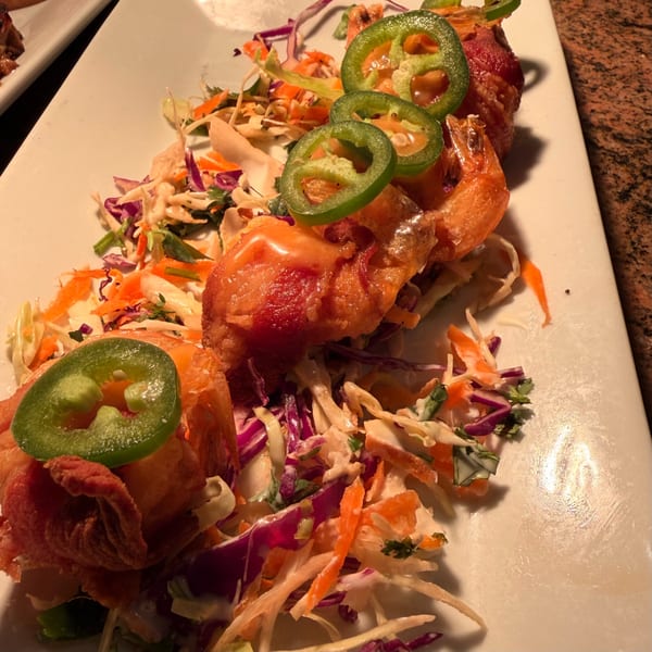 Bacon-wrapped shrimp with jalapeño slices and coleslaw on a white rectangular plate.