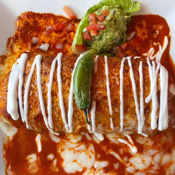 A large Anejo Cantina and Grill burrito covered in red sauce, sour cream, and a green chili.
