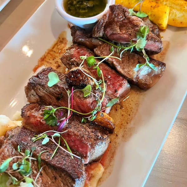 Anejo Cantina's sliced steak with green sauce, roasted garlic, and microgreens on a white plate.