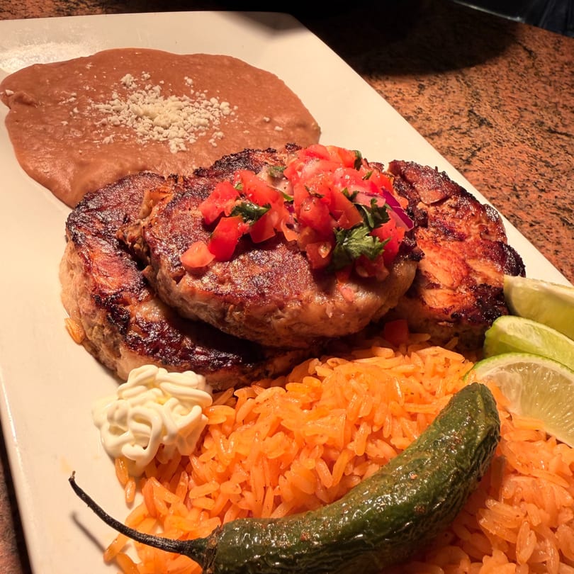 Grilled steak topped with pico de gallo, served with rice, refried beans, and lime wedges.